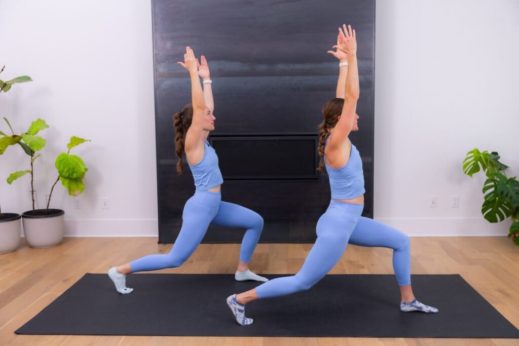 two women holding a low lunge with arms overhead in a no equipment pilates workout