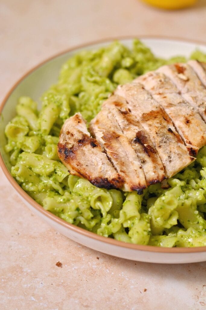 High Protein Pesto Pasta with Chicken made with green sauce in a white bowl.