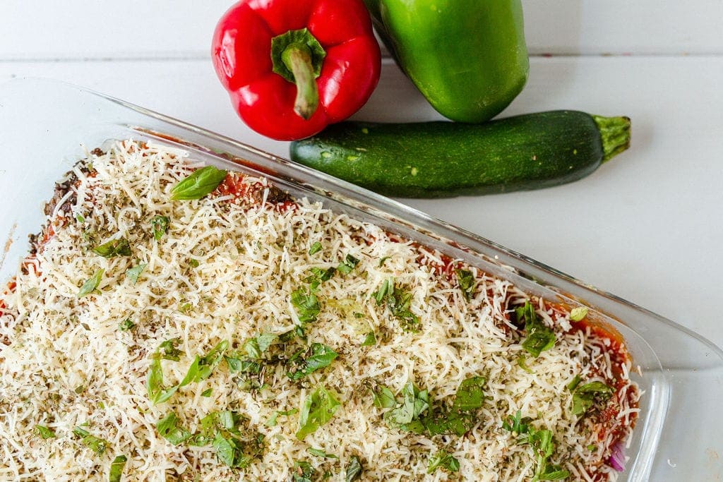 Italian Beef Quinoa Bake topped with cheese and parsley in a glass pan with red peppers, green peppers and zucchini. 