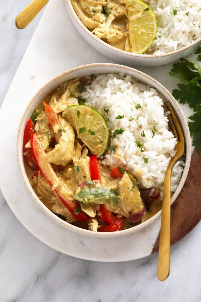Slow Cooker Coconut Chicken Curry with shredded chicken, white rice, fresh herbs, red peppers, lime slices. 