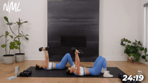 women laying on the ground performing skull crushers with dumbbells