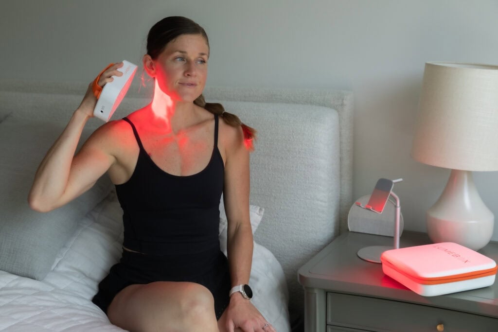 Woman demonstrating how to use the lumebox red light therapy device on her neck as biohacking for women to help with skin, joints, soreness and recovery