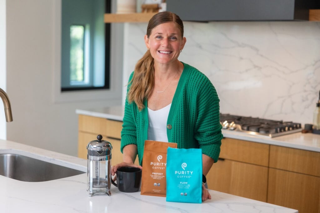 woman smiling with french press and two bags of coffee beans on counter