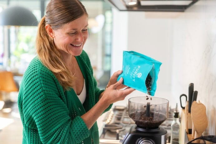 woman pouring coffee beans into grinder to make coffee before workout