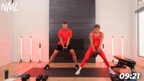 fit couple performing a lateral squat with single heavy dumbbell as part of leg and glute workout at home