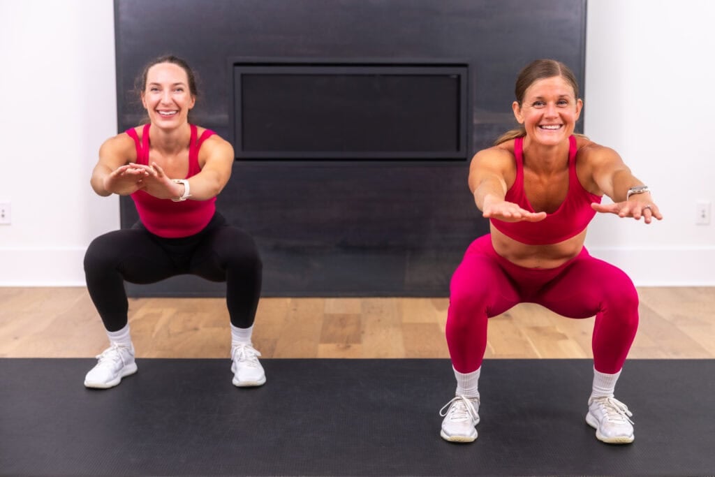 two women on black exercise mat performing an air squat as part of 5 minute workout