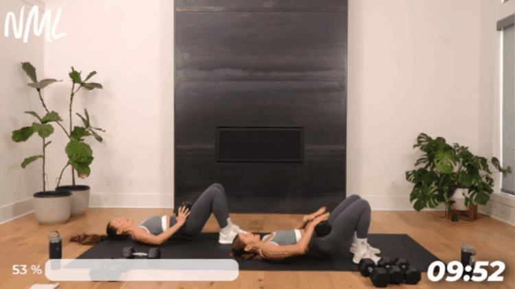 2 women performing a dumbbell glute bridge on a black exercise mat