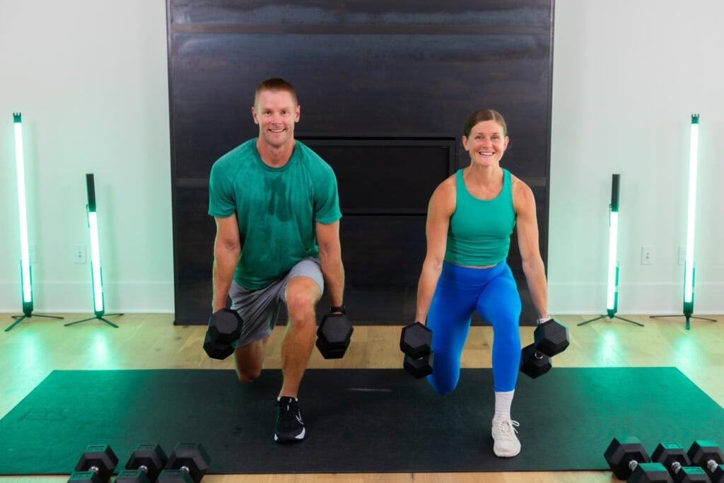Male and female doing a lunge hold with dumbbells at their sides as part of a legs and glutes drop set workout. 