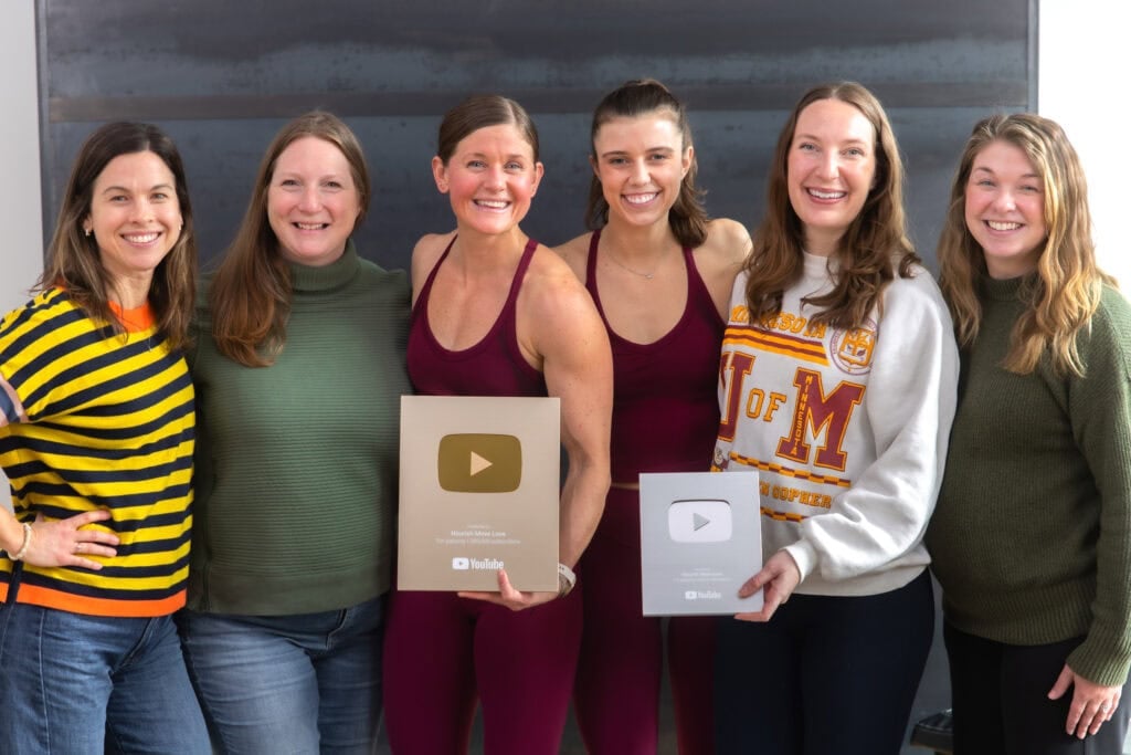 Nourish Move Love team of six women who work at Nourish Move Love full time holding their silver and gold YouTube plaques. 