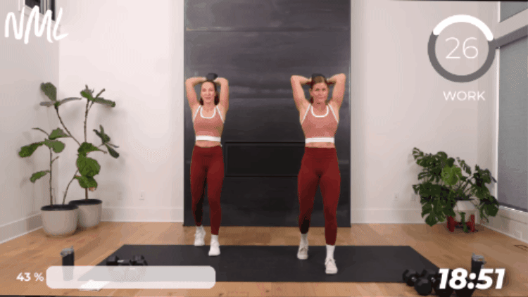 standing women performing an overhead tricep extension as part of full body dumbbell workout