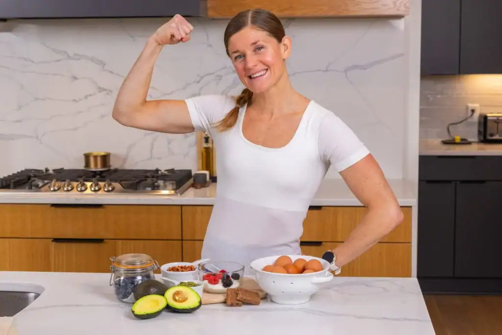 Women in her kitchen with high fiber breakfast recipe ingredients including avocado, eggs, berries, nuts, and yogurt. 