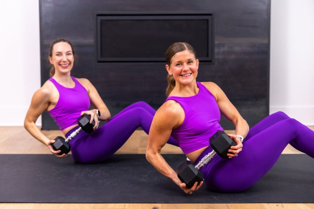 two women performing a seated twist with a dumbbell as part of full body strength workout