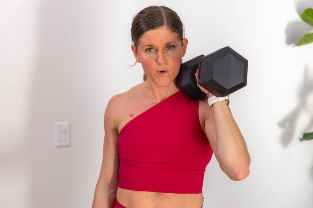 woman holding one dumbbell front racked at shoulder height as part of a functional training program