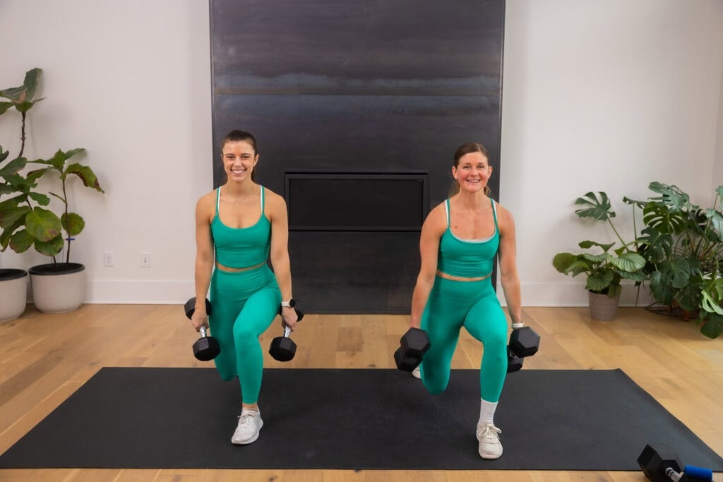 two women performing a reverse lunge with dumbbells in a leg workout