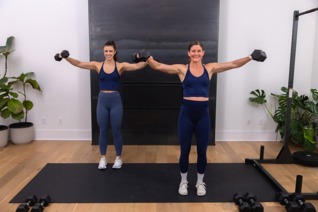 Two women performing a lateral raise as part of a back and arm workout.