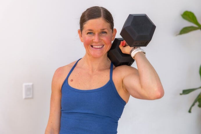 woman holding one dumbbell racked at her shoulder in a functional strength training workout