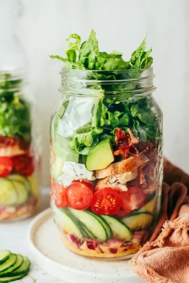 Mason Jar Chicken Avocado Club Salad with dressing, onion, cucumbers, tomatoes, blue cheese, chicken, avocado, bacon and greens.