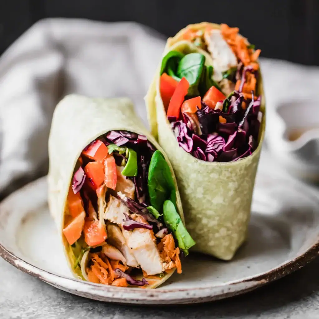 Rainbow Thai Peanut Chicken Wraps with chicken, Cabbage, carrots, tomatoes, and a wrap.