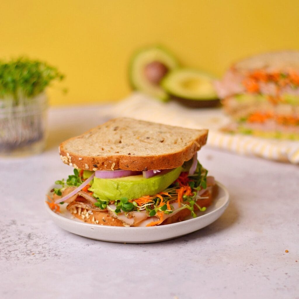 turkey avocado sandwich with turkey, onions, greens, carrots, avocado and brad.