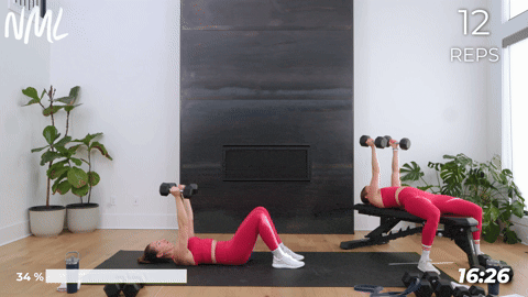 One women performing skull crushers laying on the floor and one women performing skull crushers on a bench.