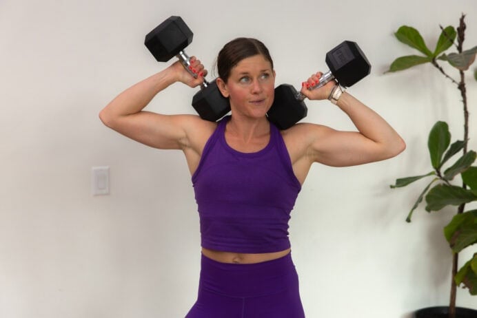 A woman holding two dumbbells over she sholders